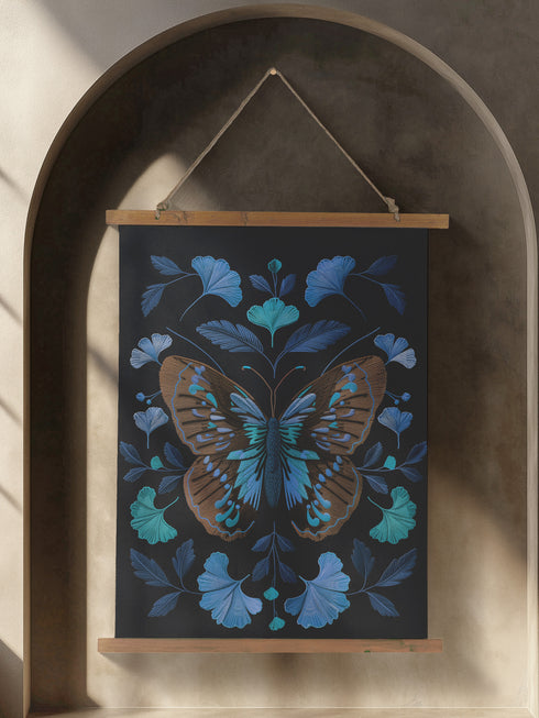 Wall hanging tapestry featuring a large copper butterfly with turquoise and azure blue markings surrounded by blue ginkgo leaves on black background. The textile hangs from wooden dowels with twine, showing detailed 3D embroidery-like texture.